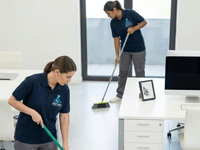 Dues treballadores amb polo blau marí fregant i escombrant el terra d’una oficina